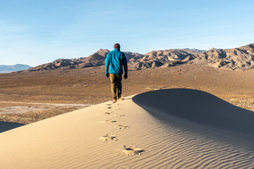 A hiker person man hiking on a sand dune leaving a track as he goes with a ridgeline clearly visible, no wind, Eureka Dunes, Death Valley National Park, California