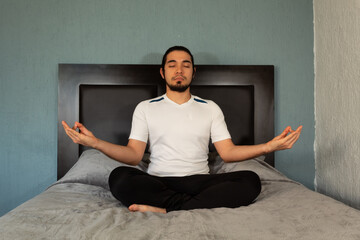 Young hispanic man with sportswear practicing yoga and meditation in his bed very calm and peaceful