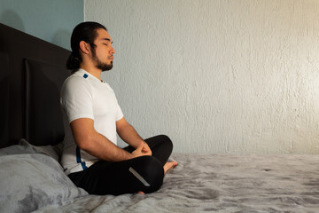 Young hispanic man with sportswear practicing yoga and meditation in his bed very calm and peaceful