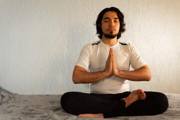Young hispanic man with sportswear practicing yoga and meditation in his bed very calm and peaceful