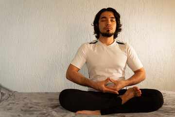 Young hispanic man with sportswear practicing yoga and meditation in his bed very calm and peaceful