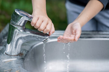 Baby try to turn off water faucet but water still leak. A child's hand turning off the tap. Save...