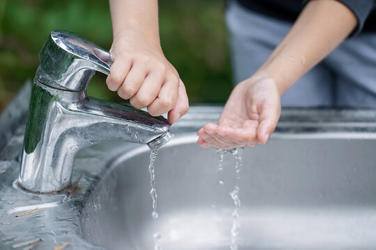 Baby Try To Turn Off Water Faucet But Water Still Leak. A Child's Hand Turning Off The Tap. Save Water. World Water Monitoring Day. Environment And Health Care Concept. Natural Green Background