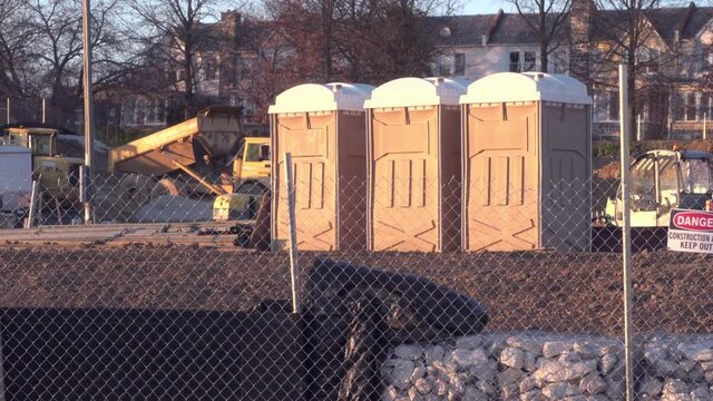 Trio of temporary placed plastic portable toilets for on site construction area work force skilled laborer crew during overtime weekend hours on weekly company paycheck