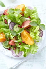 Salad with red and yellow Tomatoes and Pomegranate Seeds on bright wooden Background. Healthy Snack Idea. Top view.