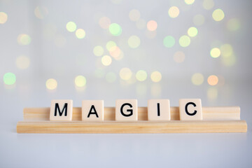 the word magic spelled out in scrabble tiles against a white background and fairy lights