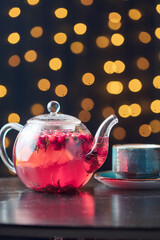 red tea with berries in a glass teapot and a blue cup on a wooden table