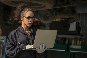 Latin-American female mechanic in a bear suit holds a laptop, inspects the engine, maintains the...