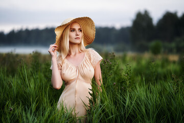 A beautiful girl stands in the tall grass and looks into the distance