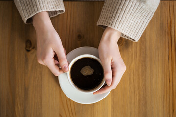 Coffee in the hands of a girl on a wooden table