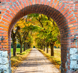 Brick arch and entrance to countryside gravel road among autumnal oak trees