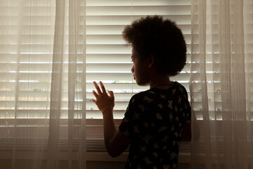 Silhouette of young girl with an afro haircut looking out through the blinds..