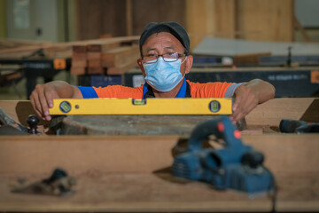 Front view photo of focused professional hardwood worker making slab coffee table use spirit level to test surface flatness .Woodworking and carpentry production
