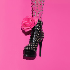 Fashion leg in heel black boots and pink roses on minimal pink background. Stylish accessories...