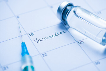 Vaccination concept. Close up view photo of vial with drugs needle of syringe and word vaccination written in calendar cell