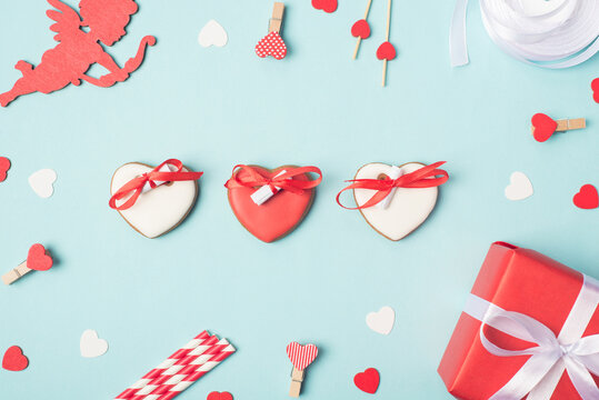 Flatlay close up photo image of yummy cookies in shape of hearts with wishes on rolled papers on blue desk with gift package little heart pins
