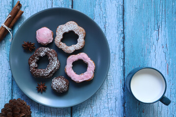 old fashion homemade chocolate and strawberry donuts in round blue ceramic plate on the vintage wooden table with a cup of milk during breakfast