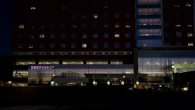 Modern hospital exterior establishing shot at night with a red emergency sign