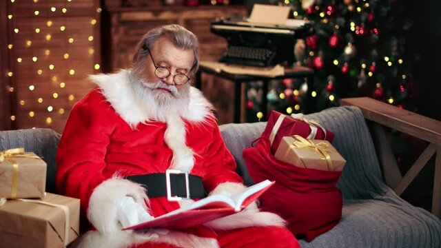 Santa Claus in festive costume natural beard reading children wish list book. 4k Dragon RED camera