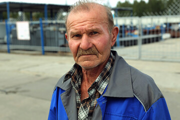 A tired and sad old man in work clothes looks at the camera. Portrait of an old and despondent...