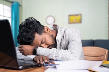 Young man got tired of working and slept on desk - Exhausted millennial fall asleep after after reading on laptop - Concept of napping at workplace and over work hours