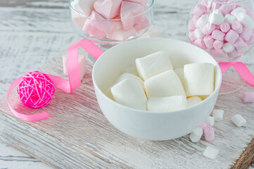 Bowl with tasty marshmallows and pink ribbon on white table, closeup