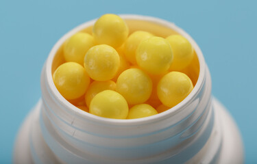 Vitamins of yellow color in the form of round dragees in a white jar on a blue background.