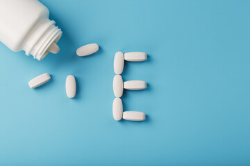 Vitamin E pills fell out of a white jar on a blue background. The letter E is an inscription.