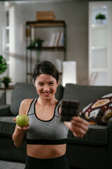Fototapeta na wymiar Young woman holding an apple and a chocolate bar. Fitness woman choosing between eating healthy or chocolate