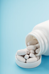 Vitamins and minerals in white capsules fell out of a white jar on a blue background.