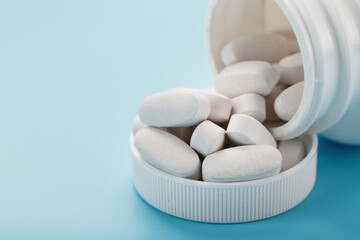 Vitamins and minerals in white capsules fell out of a white jar on a blue background.
