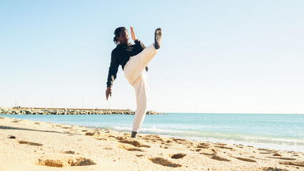 Afro man with dreadlocks training martial arts on a beach launching a kick. Personal motivation, self defense