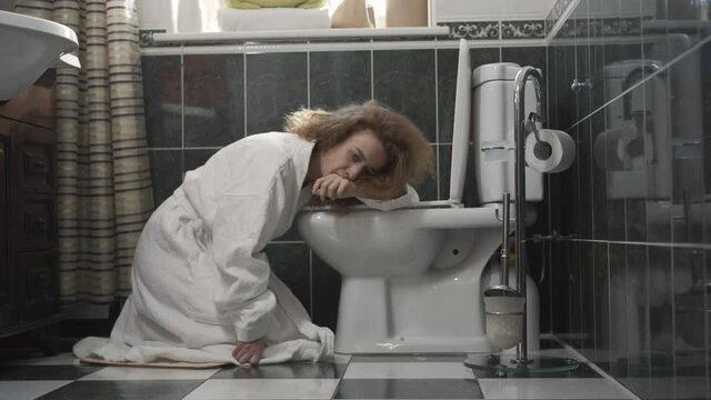 Ill or pregnant Caucasian woman sitting on the floor in toilet. Portrait of redhead lady feeling bad in bathroom at home. Vomiting and nausea. Symptoms of illness or pregnancy.