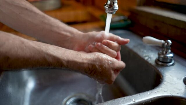 Man washing his hands thoroughly under running water in a sink