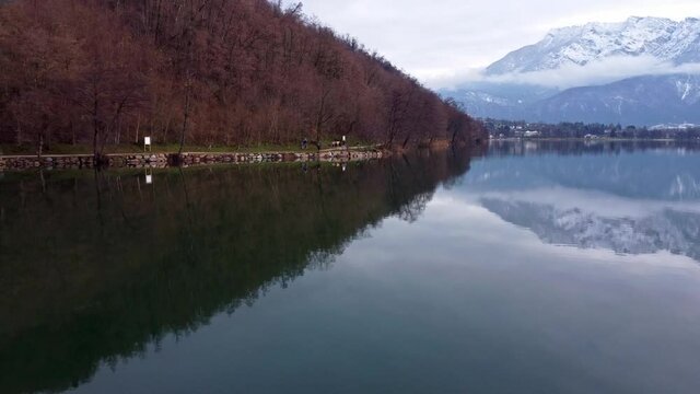 Drone aerial video footage above the Levico lake, facing the mountain Pizzo di Levico, with Forte Spitz Vezzena on the very top. Flying above the water