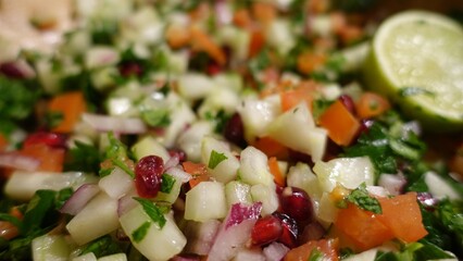 A salad with pomegranate, red onion, apple, cucumber, parsley, tomatoes and lime