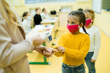 Students wearing medical masks wait in line to take the temperature at school