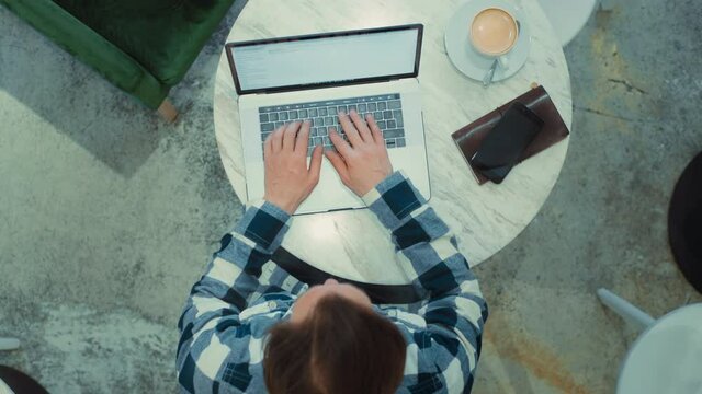 Top View On Middle Aged Adult Man Sitting At Cafe, Working On Laptop, Remotely From Outside The Office. Zoom Out Shot Of Freelancer Working. Work From Home Or From Coworking Modern Space