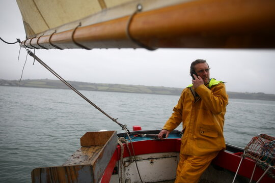 Oyster fisherman Adam Spargo speaks to a shellfish exporter on the phone after dredging for oysters on his traditional, sail-powered boat "Mistress" in the Fal Estuary