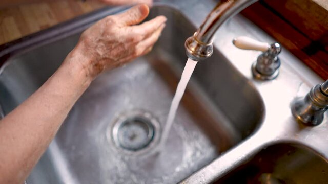 Woman washing her hands in a stainless steel sink in slow motion