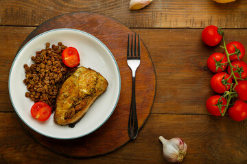 A plate of fish with lentils and tomatoes on a round stand with a fork near cherry tomatoes and lemon.