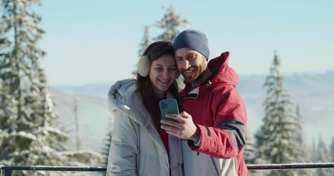 Happy holiday couple of caucasian man and woman taking photo selfie on mobile phone enjoying winter travel to the mountains.