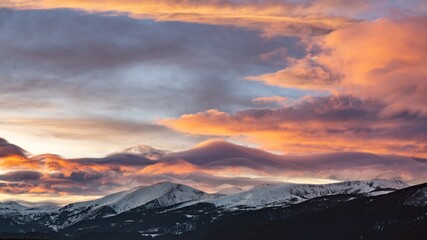 Sunset over snowy peaks in Rila Mountain, Bulgaria. Attractive orange cloudy sky, white slopes, natural landscape panoramic view. Perfect winter conditions for travel, sport recreation and tourism.