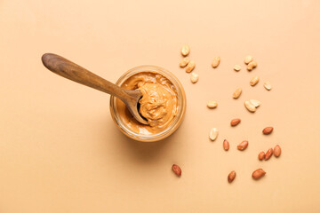 Bowl with tasty peanut butter and spoon on color background