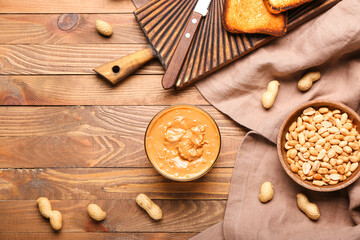 Bowl with tasty peanut butter on wooden background