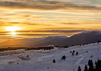 Sunset over snowy peaks in Rila Mountain, Bulgaria. Attractive orange cloudy sky, white slopes, natural landscape panoramic view. Perfect winter conditions for travel, sport recreation and tourism.
