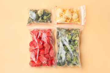Plastic bags with frozen vegetables on color background