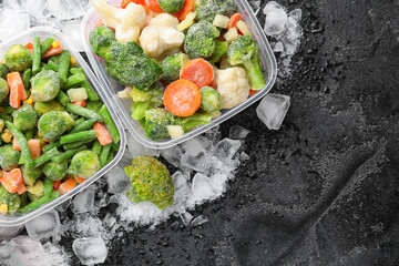 Plastic containers with frozen vegetables and ice on dark background