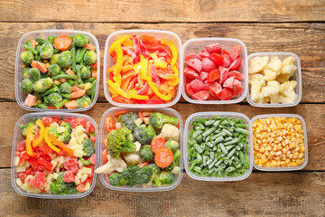 Plastic containers with frozen vegetables on wooden background