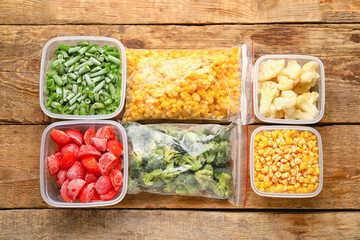 Plastic containers and bags with frozen vegetables on wooden background